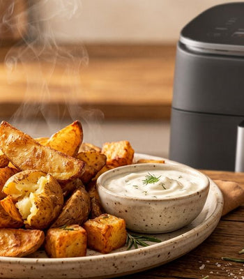 Dampfende, knusprige Kartoffelspalten und Dip neben einem schwarzen COSORI Airfryer